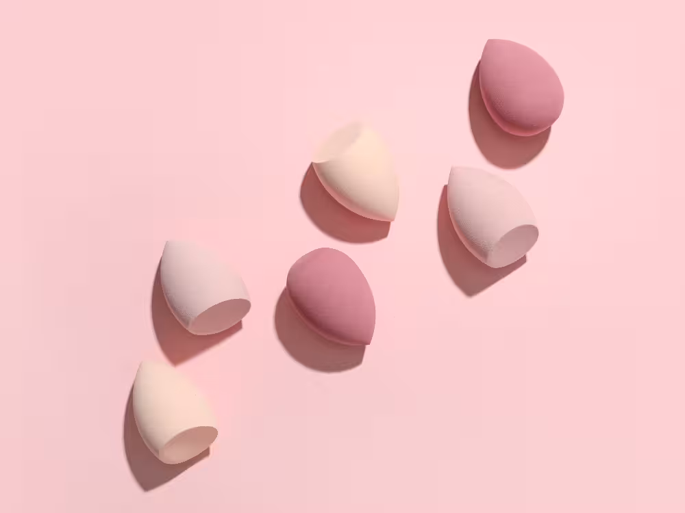 Cinco beauty blenders em tons de rosa pastel dispostas sobre fundo rosa claro, flat lay minimalista de esponjas de maquiagem
