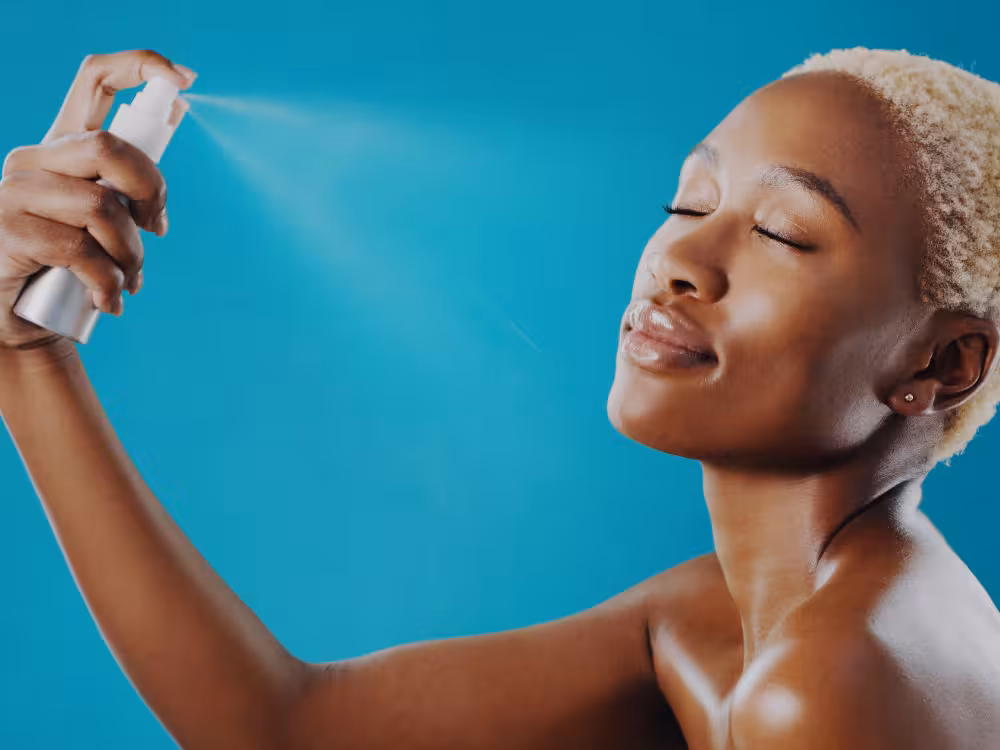 Close de mãos femininas segurando um frasco de protetor solar na areia da praia. Uma mão está despejando o creme na outra, ilustrando o passo essencial de reaplicação do FPS durante o dia no verão para garantir a proteção total da pele.