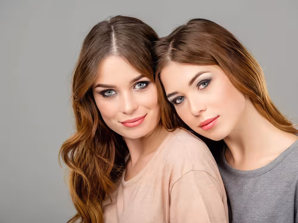 Duas meninas de pele branca, cabelos em tom castanho e pontas loiras, olhos esverdeados. As duas estão com o rosto maquiado.