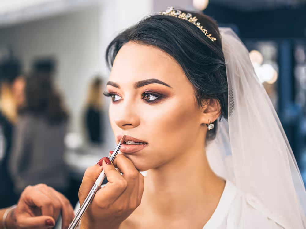 Noiva linda, com véu, maquiada por uma maquiadora para seu casamento
